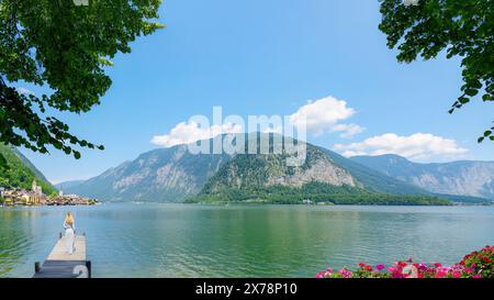 Hallstatt, Austria, 18 maggio 2024 - Una donna gode di una vista panoramica da cartolina del famoso villaggio di Hallstatt che si riflette sul lago Hallstattersee Foto Stock