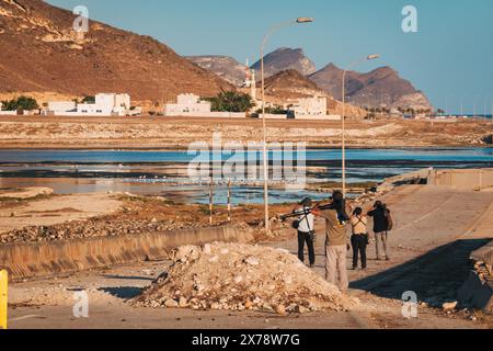 Gli osservatori di uccelli scattano foto al ponte rotto presso al Mughsail Beach in Oman, con montagne aspre e mare sullo sfondo. Foto Stock
