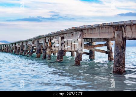 Foto di un molo di legno che si estende fino al mare. Bella vista laterale del molo. Calme acque turchesi, struttura a ponte in legno e cielo meraviglioso. Foto Stock