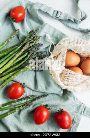 Accanto a un sacchetto in rete riutilizzabile ripieno di uova marroni, impreziosito da pomodori ciliegini maturi su una superficie di colore chiaro con una Foto Stock
