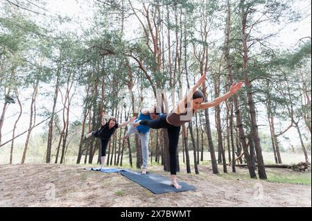 Un gruppo di tre persone che fanno yoga nella foresta. Un uomo e due donne in posa da guerriero. Foto Stock