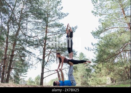 Tre amici praticano esercizi di acro yoga mentre fanno trekking nella foresta. Foto Stock