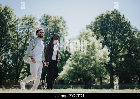 Coppia gay multirazziale che si gode una giornata di sole insieme nel parco, tenendosi per mano e sorridendo Foto Stock