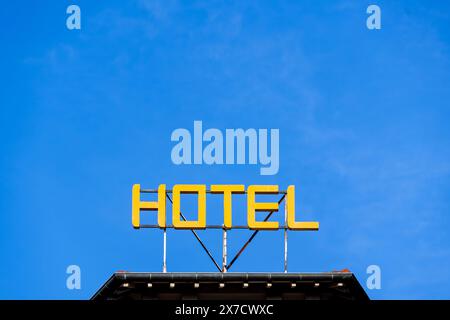 Cartello con la parola "HOTEL" scritta in lettere maiuscole gialle luminose sul tetto di un edificio su uno sfondo blu del cielo. Spazio negativo Foto Stock