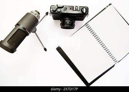 fotocamera, microfono e blocco note su uno sfondo bianco pulito. Perfetto per rappresentare la creazione di contenuti, il vlogging, il giornalismo o la scrittura. Foto Stock