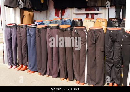 Una fila di manichini che mostrano diversi stili di pantaloni, tra cui jeans e pantaloni casual, allineati in un mercato all'aperto durante il giorno, ciascuno Foto Stock