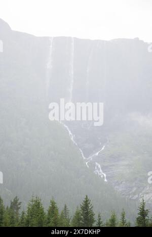 Enorme cascata che cade da un picco di montagna norvegese in un giorno d'estate nebbioso e piovoso. Foto Stock