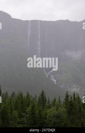 Enorme cascata che cade da un picco di montagna norvegese in un giorno d'estate nebbioso e piovoso. Foto Stock