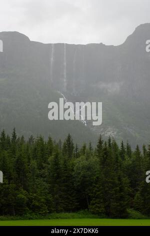 Enorme cascata che cade da un picco di montagna norvegese in un giorno d'estate nebbioso e piovoso. Foto Stock