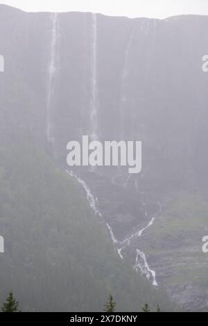 Enorme cascata che cade da un picco di montagna norvegese in un giorno d'estate nebbioso e piovoso. Foto Stock