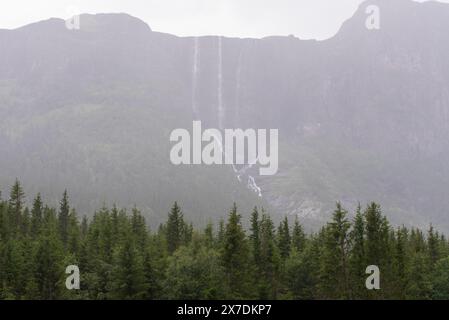 Enorme cascata che cade da un picco di montagna norvegese in un giorno d'estate nebbioso e piovoso. Foto Stock