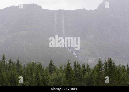 Enorme cascata che cade da un picco di montagna norvegese in un giorno d'estate nebbioso e piovoso. Foto Stock