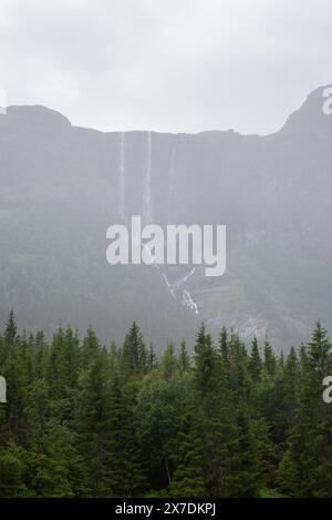 Enorme cascata che cade da un picco di montagna norvegese in un giorno d'estate nebbioso e piovoso. Foto Stock