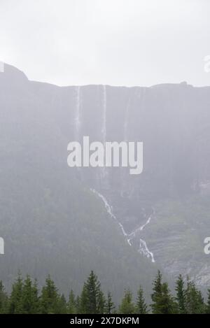 Enorme cascata che cade da un picco di montagna norvegese in un giorno d'estate nebbioso e piovoso. Foto Stock