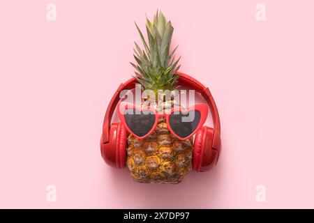 Ananas fresco con occhiali da sole e cuffie su sfondo rosa Foto Stock