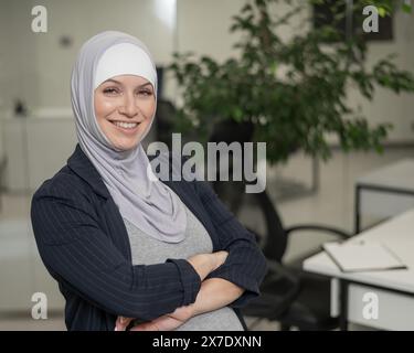 Donna caucasica incinta in hijab che lavora in ufficio. Foto Stock