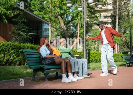 Uno studente di nero felicissimo si allunga di mano a cinque per gli amici che si rilassano sulla panchina del campus universitario Foto Stock