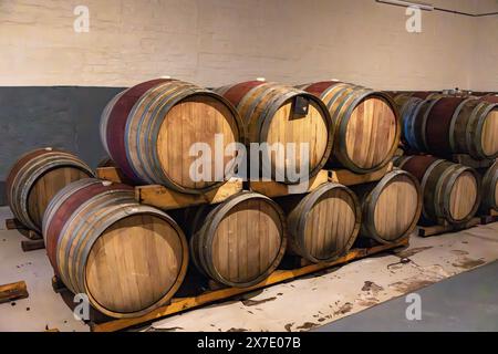 Le botti di vino di rovere impilate l'una sull'altra invecchiano in una cantina. Foto Stock