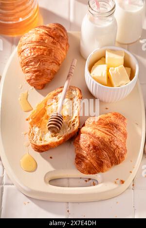 Croissant francesi caldi e dorati nella mattina di primavera. Colazione con latte, miele e burro. Foto Stock