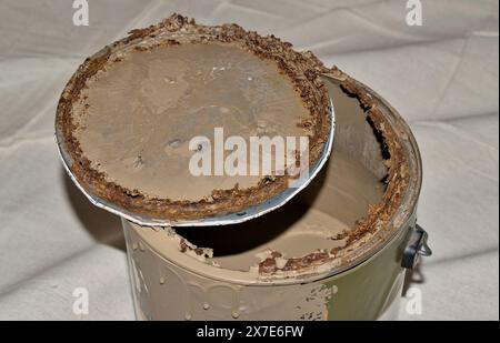 Vecchia scatola per vernice in metallo arrugginito con coperchio aperto su un panno marrone conservazione scaduta. Foto Stock