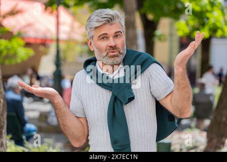 Non so cosa dire. Un uomo maturo confuso che si sente imbarazzato per una domanda ambigua, che ha dubbi, non ne ha idea, che sia insicuro all'aperto. Ragazzo adulto caucasico in piedi in città strada Foto Stock