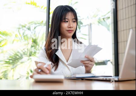 Una bella donna d'affari asiatica millenaria, professionista, o una donna contabile, sta controllando le fatture e le ricevute, lavorando sui dati finanziari aziendali su di lui Foto Stock