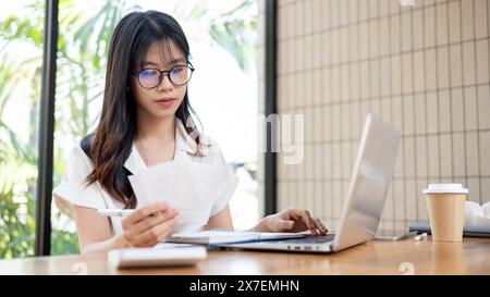 Una donna d'affari o una contabile asiatica, bella e professionale, si sta concentrando sul controllo di bollette e ricevute, lavorando sulla financia per affari Foto Stock