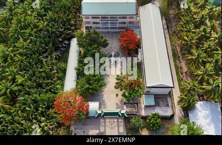 Incredibile paesaggio del villaggio del Delta del Mekong, campus scolastico con fiori rossi di fenice che fioriscono vibrante, liceo tra la foresta di cocco, sfavillante è Foto Stock