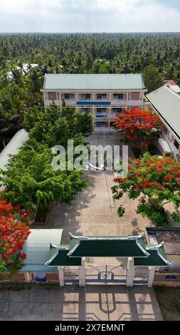 Incredibile paesaggio del villaggio del Delta del Mekong, campus scolastico con fiori rossi di fenice che fioriscono vibrante, liceo tra la foresta di cocco, sfavillante è Foto Stock