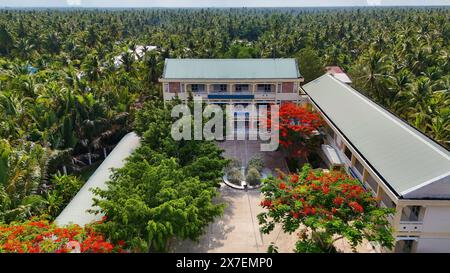 Incredibile paesaggio del villaggio del Delta del Mekong, campus scolastico con fiori rossi di fenice che fioriscono vibrante, liceo tra la foresta di cocco, sfavillante è Foto Stock