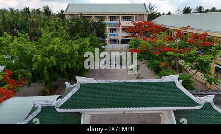 Incredibile paesaggio del villaggio del Delta del Mekong, campus scolastico con fiori rossi di fenice che fioriscono vibrante, liceo tra la foresta di cocco, sfavillante è Foto Stock