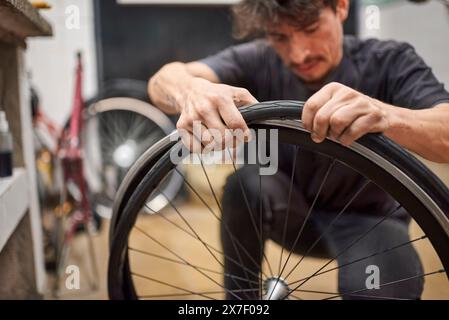 Il tecnico latino che ripara biciclette monta uno pneumatico senza aria su una ruota da bici presso la sua officina di riparazione. Composizione selettiva della messa a fuoco con spazio di copia. Foto Stock