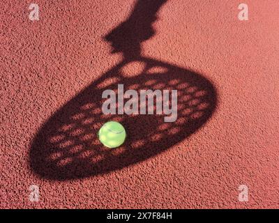 Alto angolo di palla gialla posizionato sul campo e ricoperto di ombra di una persona che tiene la racchetta del padel Foto Stock