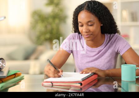 Studente nero che prende appunti apprendendo su un PC desktop a casa Foto Stock