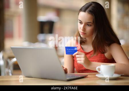 Donna seria che acquista online con carta di credito e laptop in una terrazza del ristorante Foto Stock