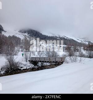 un ponte di legno attraversa il fiume nella valle innevata Foto Stock