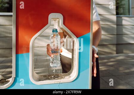 Una donna versa acqua potabile in una bottiglia d'acqua in città in un distributore di benzina. Consumo sostenibile delle risorse e riduzione dei rifiuti Foto Stock