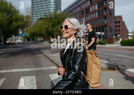 Ritratto di una donna matura elegante con i capelli grigi sulla strada della città. Donna anziana con occhiali da sole in attesa dei trasporti pubblici. Foto Stock