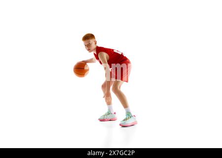 Atleta concentrato e motivato, ragazzo in uniforme rossa che pratica il basket, gioca con la palla isolata su sfondo bianco dello studio Foto Stock