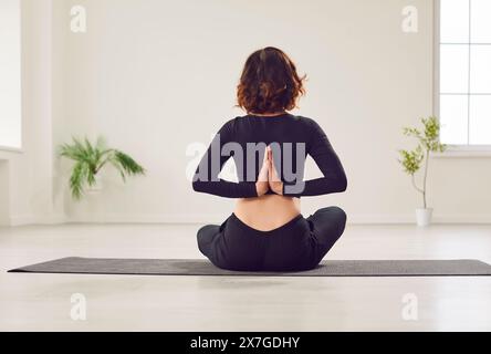 Yogi Woman vista posteriore pratica yoga, seduta nell'esercizio Ardha Padmasana, mezza posa Lotus Foto Stock