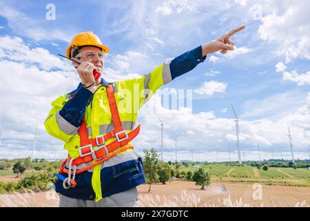 il controllo maschio dell'ingegnere opera sul campo manutenzione esterna del servizio generatore eolico. mano del lavoratore che punta la posizione al gesto dell'ordine Foto Stock