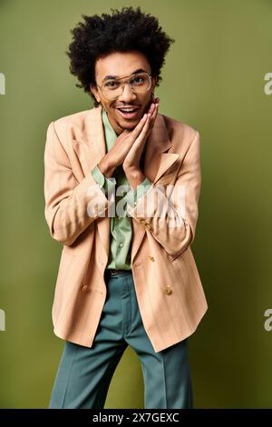 Un giovane afroamericano dai capelli ricci, vestito con un elegante vestito, cravatta e occhiali da sole, posa con fiducia per un ritratto contro un backgroun verde Foto Stock