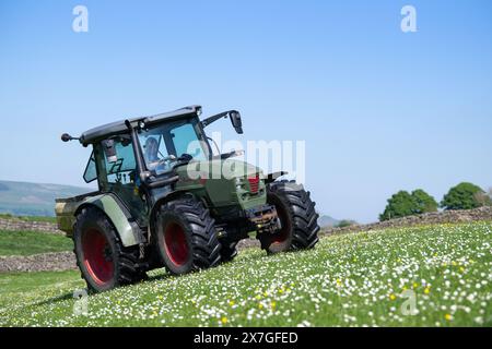 Coltivatore che spande fertilizzante su un prato di fieno tradizionale nelle valli dello Yorkshire utilizzando un trattore Hurlimann e uno spanditore Teagle fert. North Yorkshire, Foto Stock