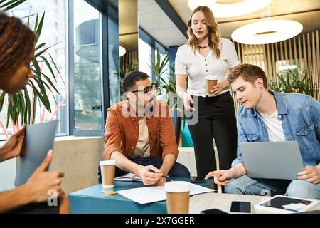 Un gruppo eterogeneo di colleghi si è impegnato in una sessione di lavoro collaborativa, seduti attorno a un tavolo, ciascuno incentrato sui propri laptop. Foto Stock