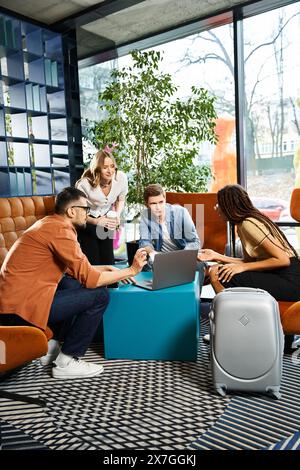 I colleghi multiculturali in abbigliamento informale si sono riuniti intorno a un computer portatile nella hall dell'hotel durante un viaggio d'affari. Foto Stock