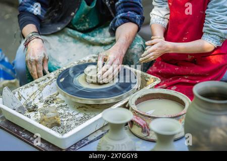 Artigiano, potter insegna al bambino a realizzare pentole di ceramica su ruote di ceramica, concetto di lavoro artigianale Foto Stock