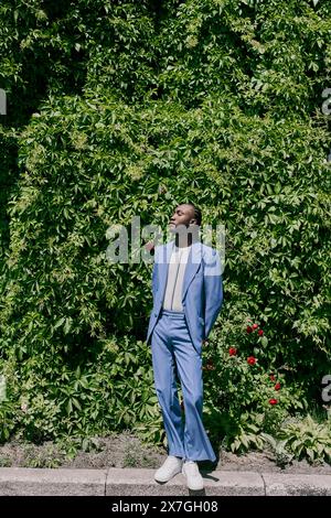 Un uomo elegante con una tuta blu si erge con sicurezza su un marciapiede della città. Foto Stock