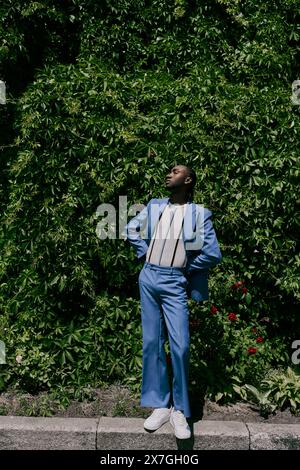 Un uomo elegante con una tuta blu si erge con sicurezza su un marciapiede urbano. Foto Stock