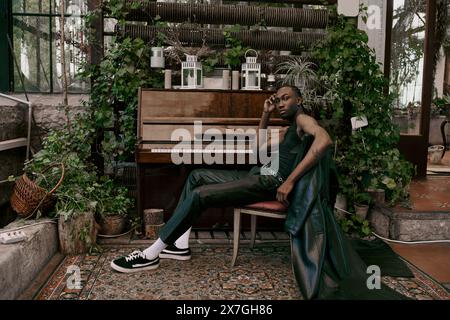 Un uomo affascinante in un abbigliamento sofisticato si siede accanto a un pianoforte a coda in un vivace giardino verde. Foto Stock