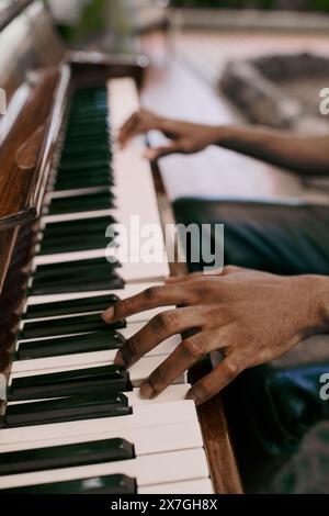 Elegante uomo afroamericano suona il pianoforte con le mani in un lussureggiante giardino. Foto Stock